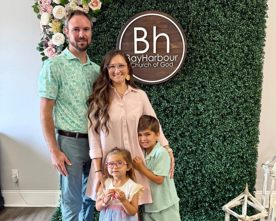 Family posing in front of a floral and greenery backdrop with 'Bay Harbour Church of God' logo.
