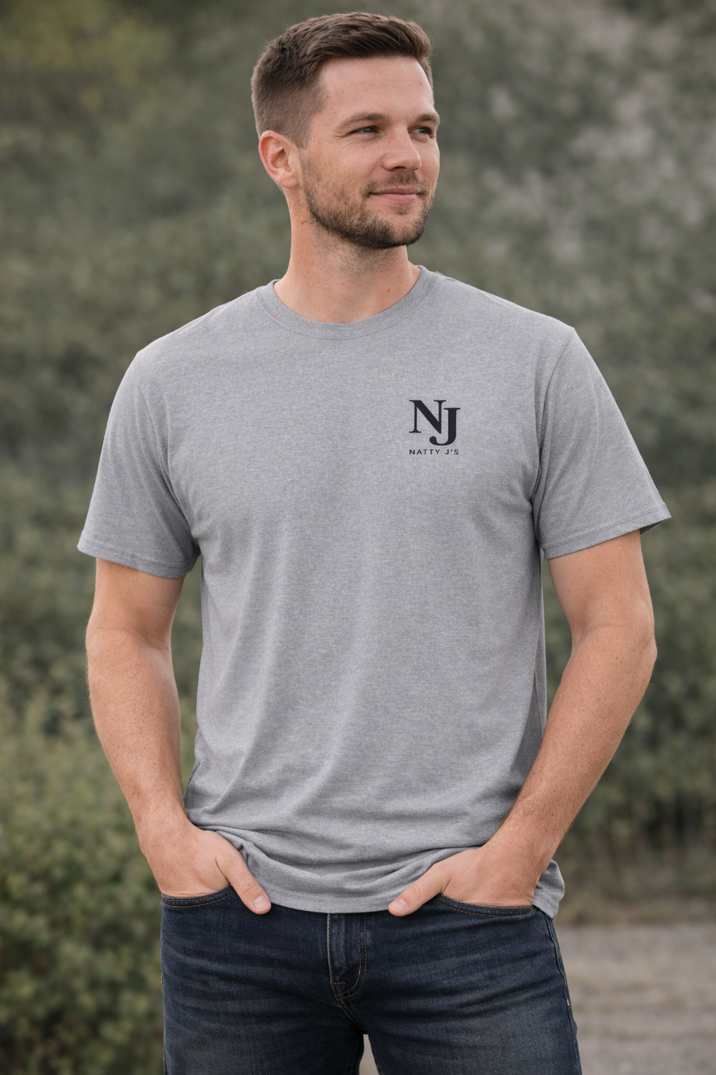 Man wearing a gray t-shirt with a logo and text, standing against a blurred natural background