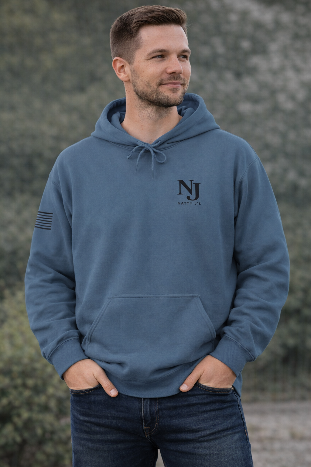Man wearing a blue hoodie with a logo, standing against a blurred natural background