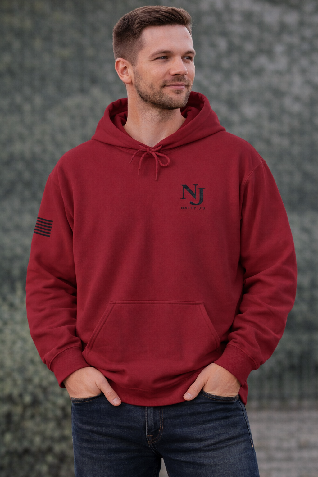 Man wearing a red hoodie with a logo, standing against a textured wall.