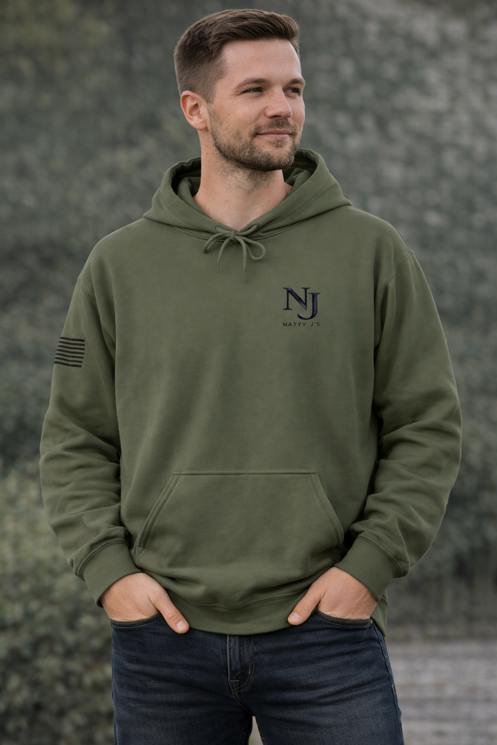 Man wearing an olive green hoodie with a logo, standing against a textured wall.