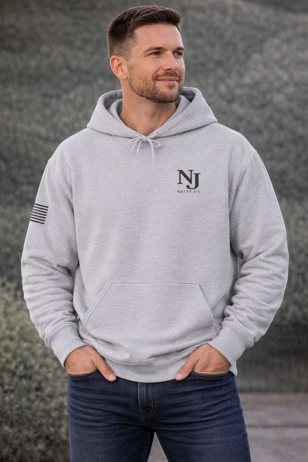 Man wearing a gray hoodie with 'NJ' logo against a textured wall.