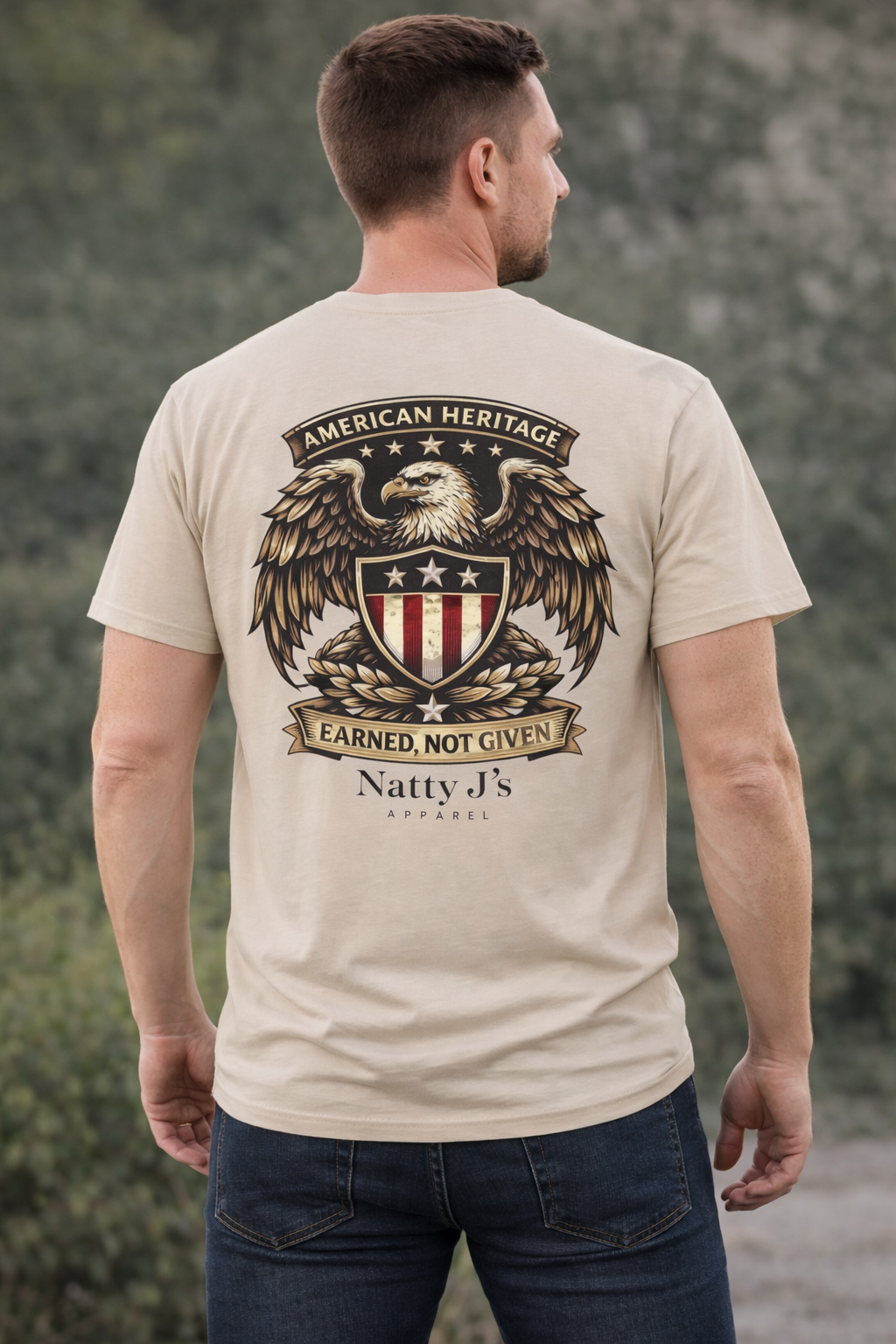 Man wearing a beige t-shirt with an eagle and shield design on the back, standing outdoors.