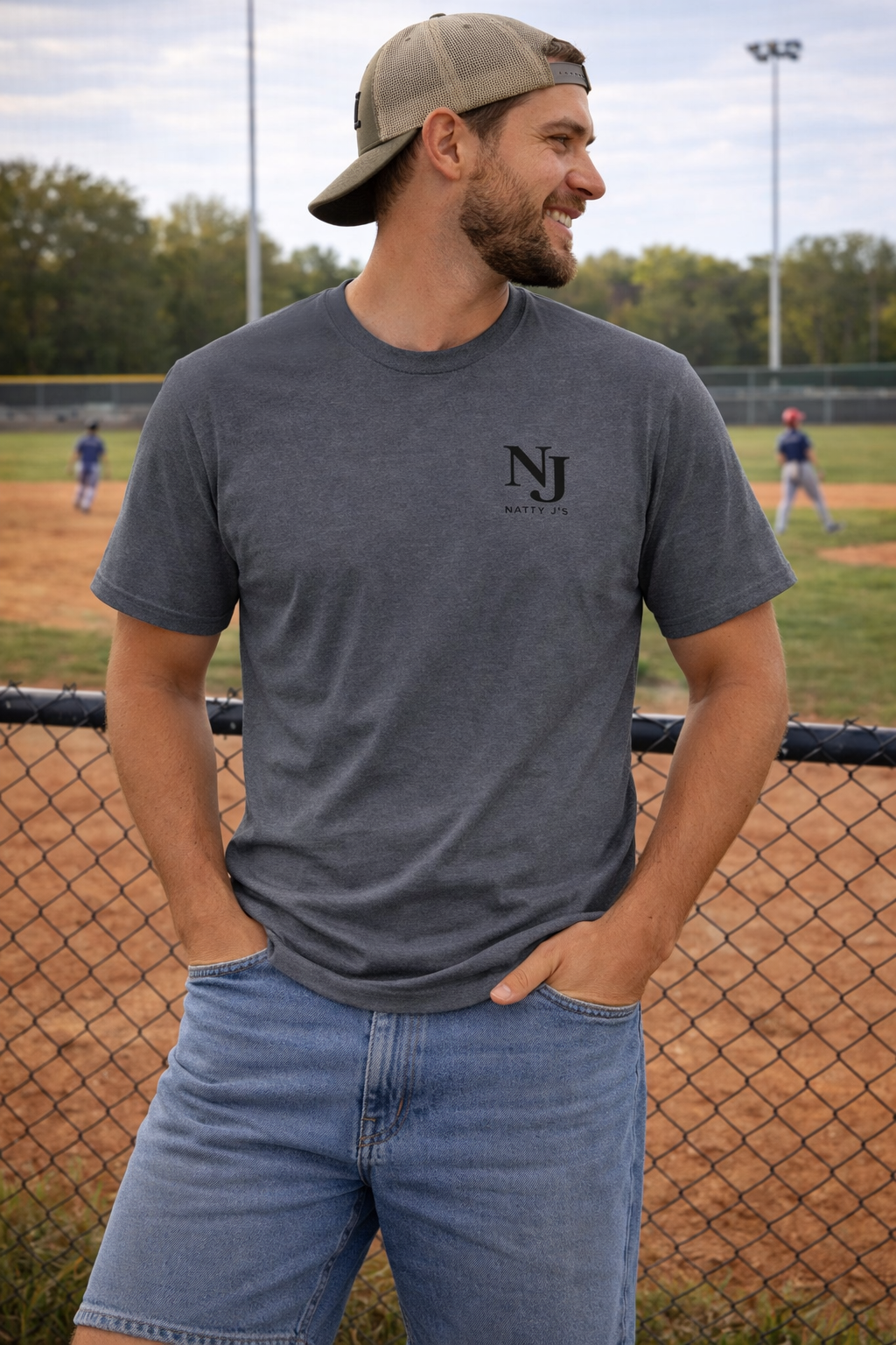 Man wearing a gray t-shirt with 'NJ' logo on a baseball field