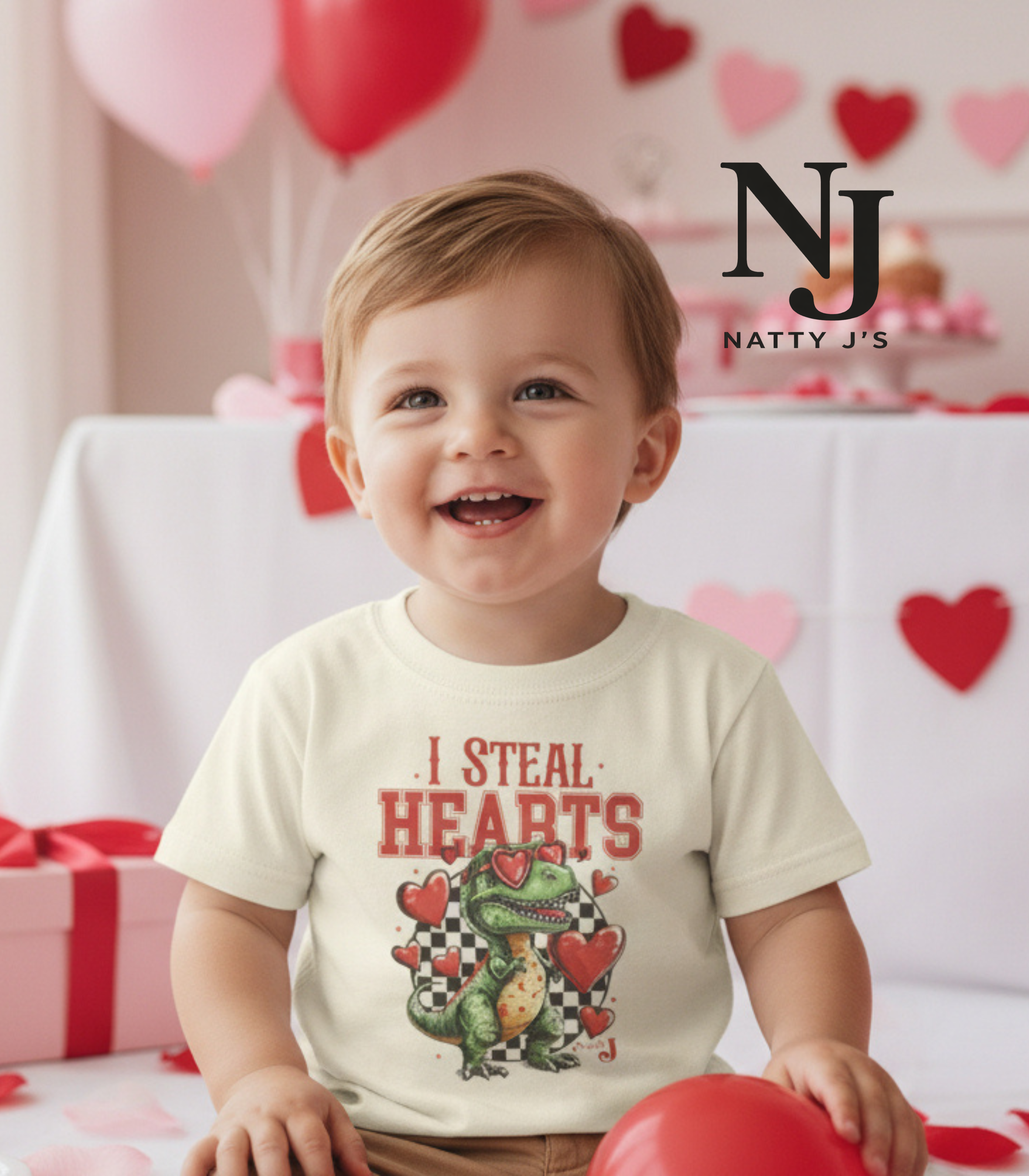 Child wearing a t-shirt with a dinosaur graphic and text, surrounded by balloons and hearts, with Natty J's branding.