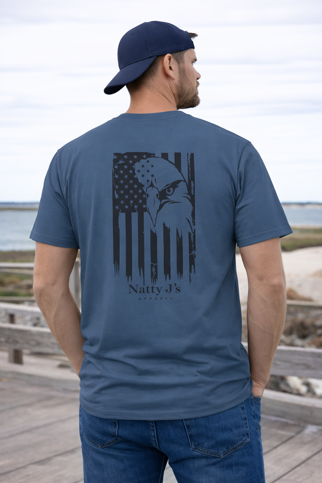 Man wearing a blue t-shirt with an eagle design and 'Natty J's' branding on a beach.