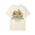 An off-white short-sleeve t-shirt with a vintage-style graphic on the front featuring two birds perched on sunflowers, with the text 'Dove Season' and 'Natty J's APPAREL' printed below.