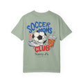A sage green short-sleeve t-shirt with a colorful graphic on the back featuring a soccer ball, cleats, a drink, and the text 'SOCCER MOMS CLUB' and 'Natty J's APPAREL'.