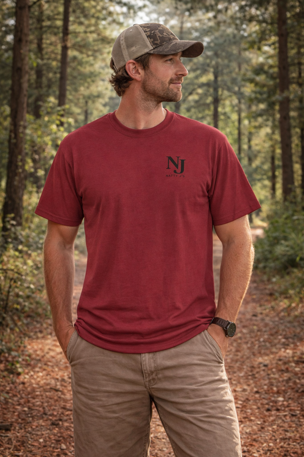 Man wearing a red t-shirt with a logo, standing in a forest.