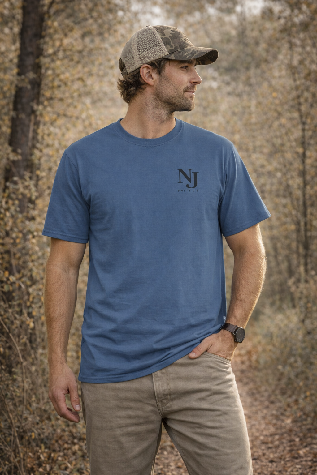 Man wearing a blue t-shirt with a logo and a cap, standing in a forested area.