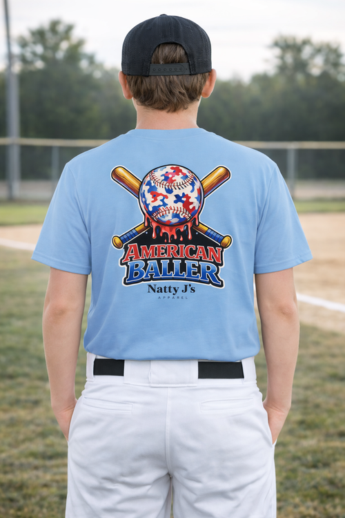 Person wearing a light blue t-shirt with 'American Baller' design on a baseball field.