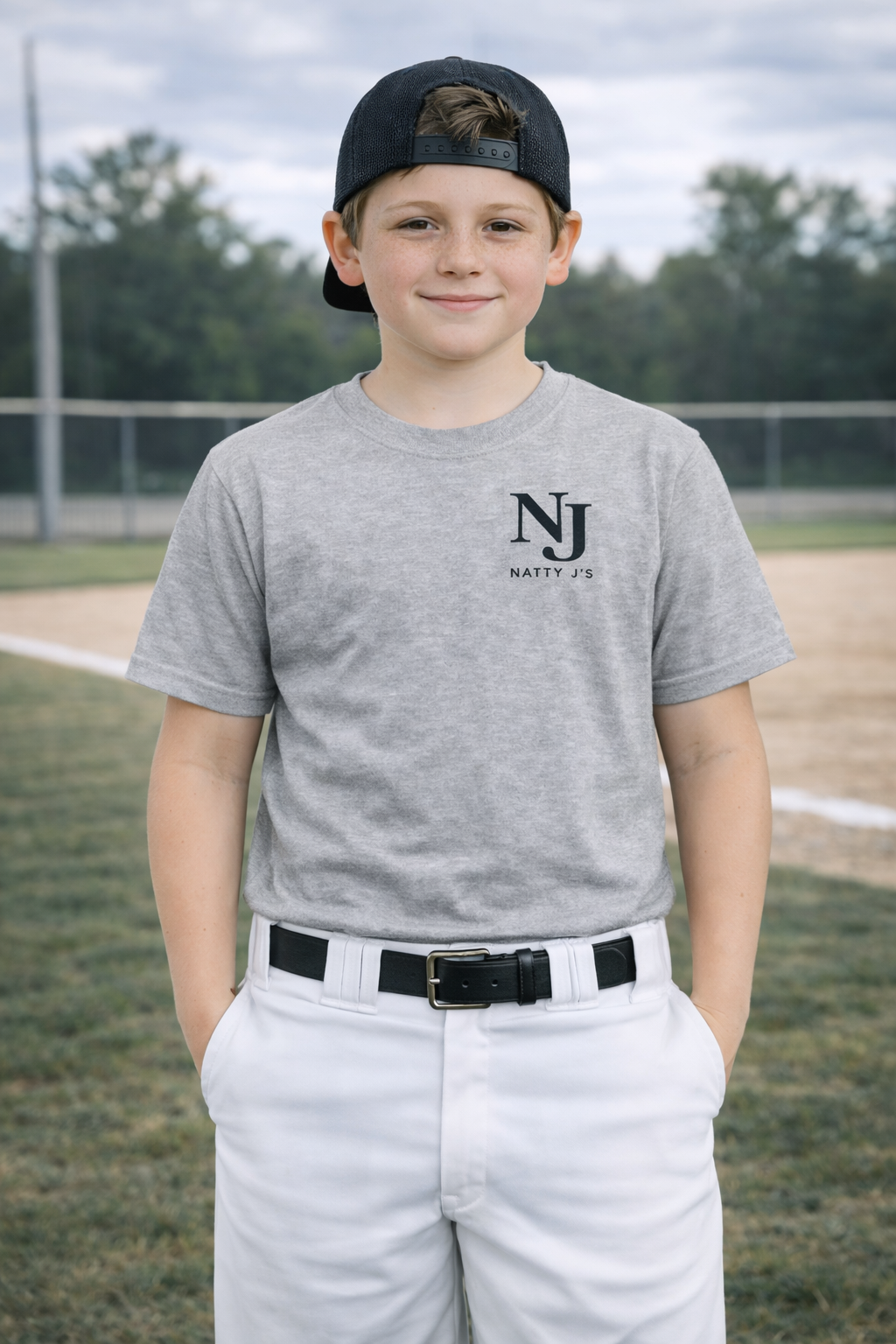 Young boy wearing a gray t-shirt with 'NJ' logo on a baseball field