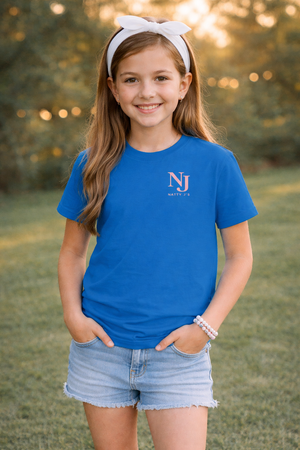 Young girl wearing a blue t-shirt with a logo, standing outdoors with trees in the background.