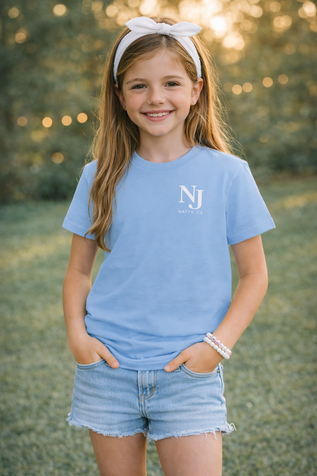 Young girl wearing a blue t-shirt with a logo, standing outdoors with a blurred natural background
