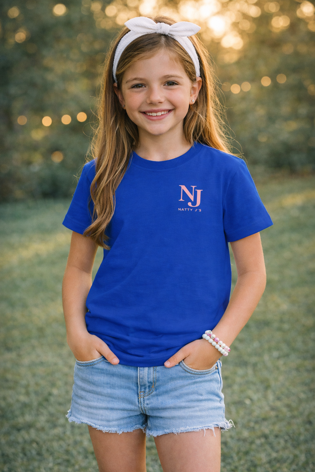 Young girl wearing a blue t-shirt with a logo, standing outdoors.