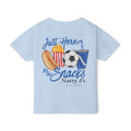 A light blue kids' t-shirt shown flat against a white background, featuring a colorful graphic print on the back with a hot dog, popcorn, soccer ball, and drink, accompanied by the text 'Just Here for the Snacks Natty J's APPAREL'.