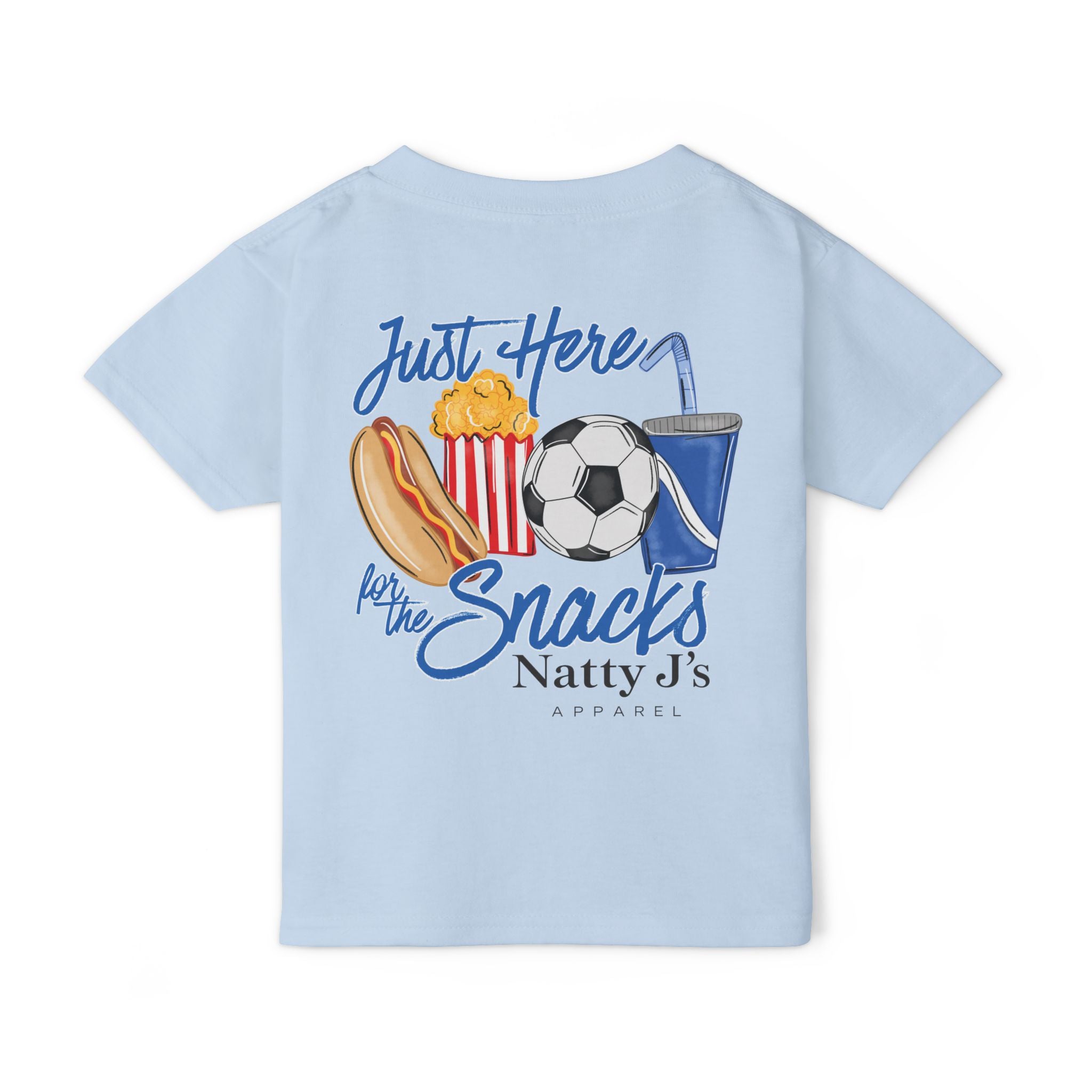 A light blue kids' t-shirt shown flat against a white background, featuring a colorful graphic print on the back with a hot dog, popcorn, soccer ball, and drink, accompanied by the text 'Just Here for the Snacks Natty J's APPAREL'.